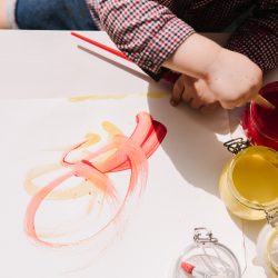 Toddler painting with red and yellow paints on white paper