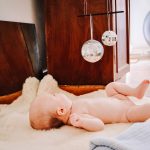 Eight week old baby lying on back on sheepskin gazing at silver baubles