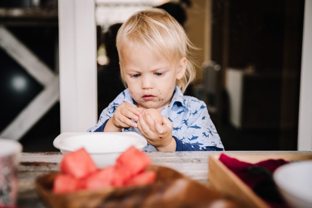Toddler sitting at table peeling a boiled egg