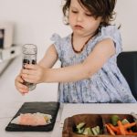 Preschooler sitting at table grinding pepper onto Vietnamese summer roll