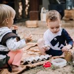 Two young children sitting on grass making a bird feeder