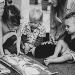 Three young children reading a book with an adult