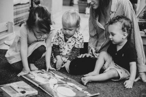 Three young children reading a book with an adult